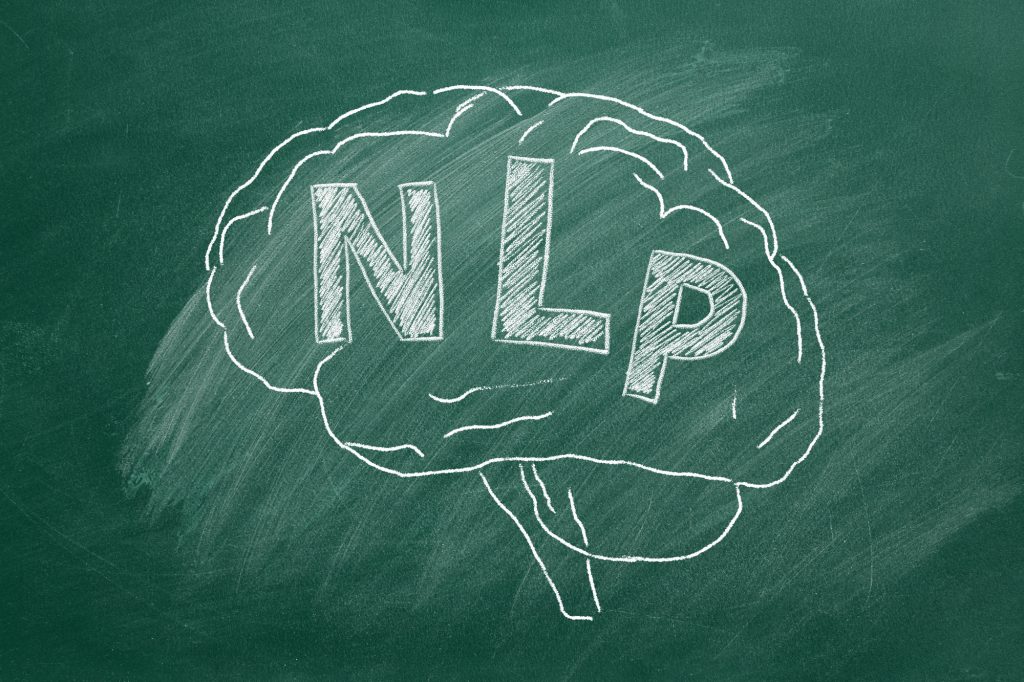 Human brain with abbreviation NLP hand drawing in chalk on blackboard. Neuro-linguistic programming.
